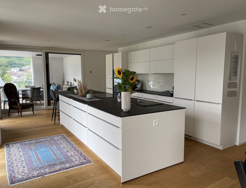 Modern kitchen with white cabinets, black countertop, island, and a view of a dining area through large glass doors.