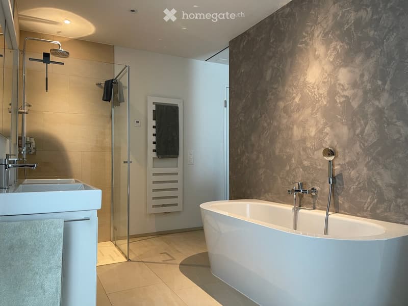 Modern bathroom with a freestanding bathtub, double sink, glass-enclosed shower, and marble accent wall.