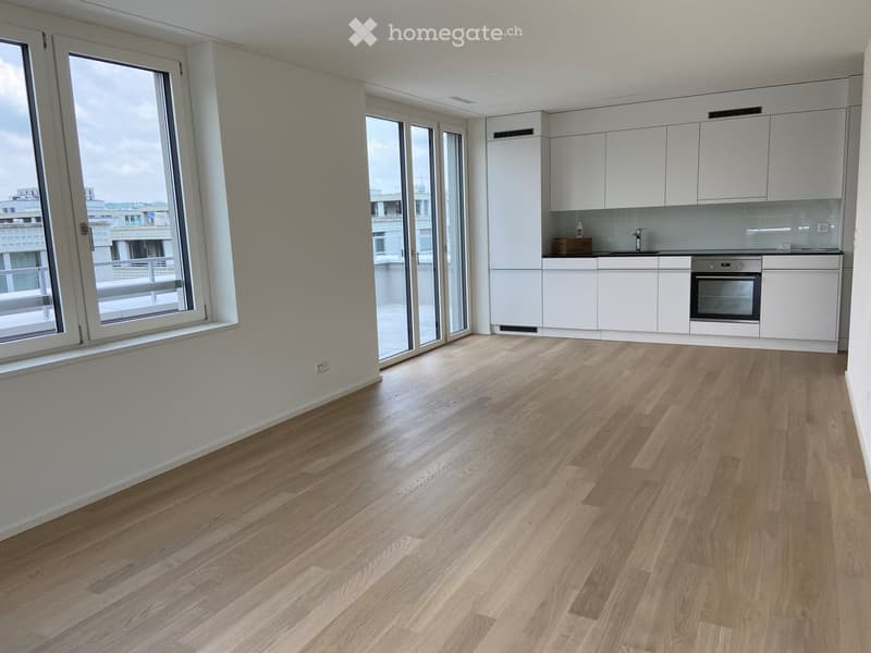 Empty kitchen with white cabinets, wooden flooring, large windows, and a small sink area.