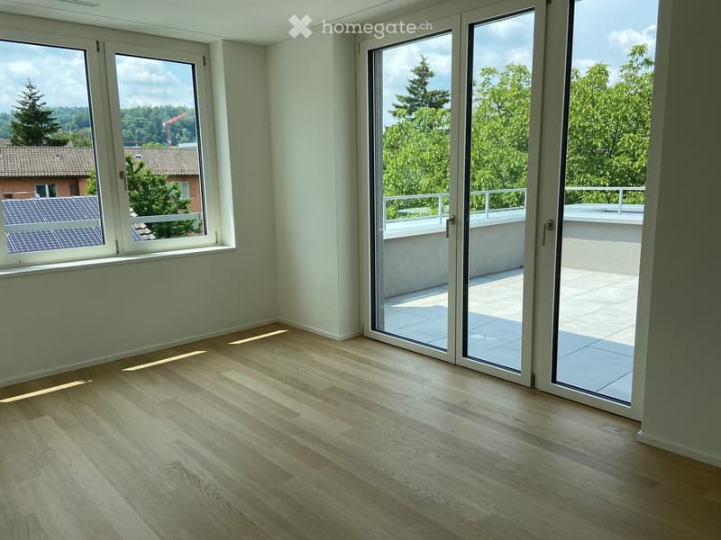 Empty room with light wooden flooring, large windows, and sliding glass doors leading to a balcony.