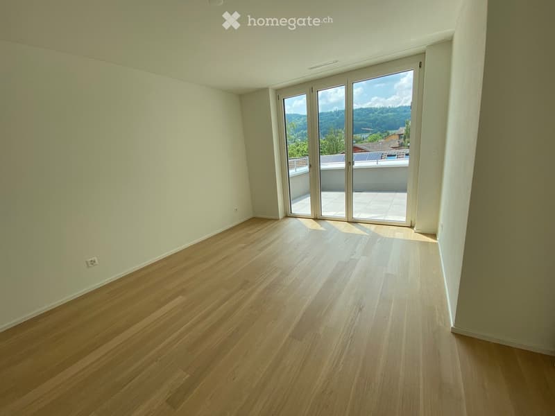 Empty room with light wooden flooring and white walls, featuring large sliding glass doors leading to a balcony with a scenic mountain view.