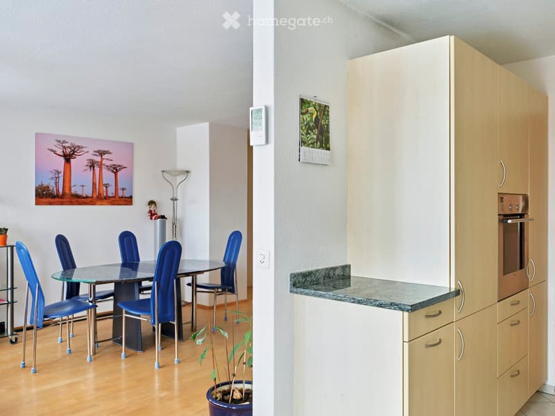 Wooden floor, dining table, blue chairs, potted plant, wall painting, kitchen cabinet, calendar, and built-in oven