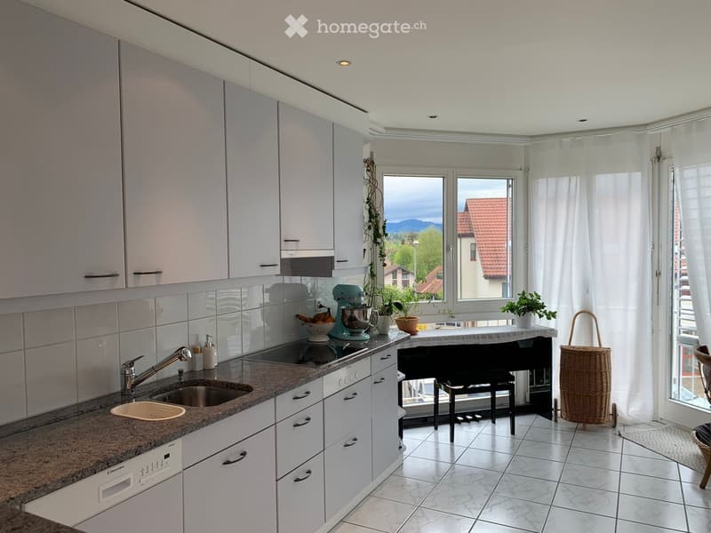 Modern kitchen with white cabinets, granite countertops, stainless steel sink, dishwasher, and various appliances. Features a large window with a view of the landscape.