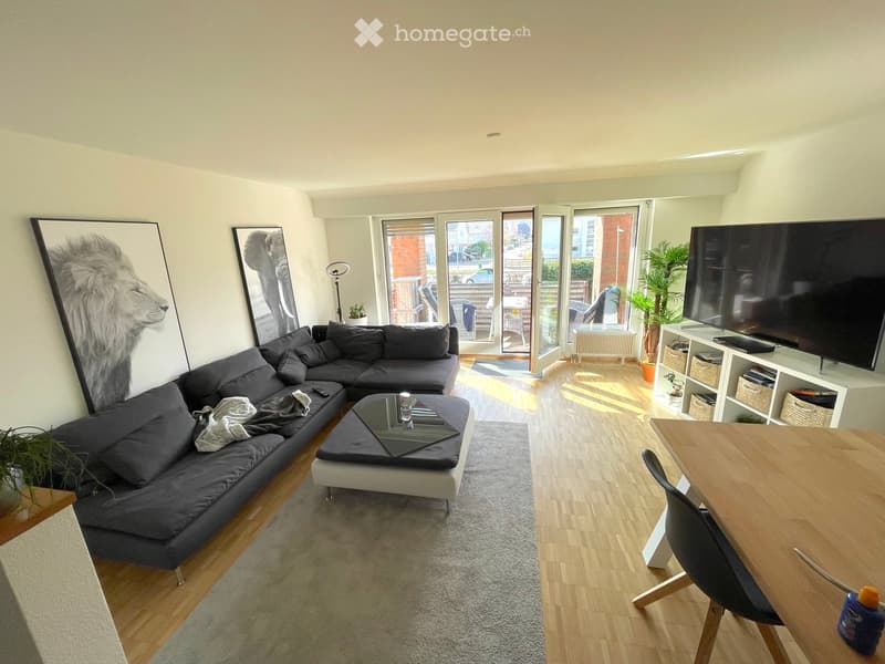 Modern living room with a grey sectional sofa, coffee table, dining table with chairs, TV, floor lamp, and artwork on the walls.
