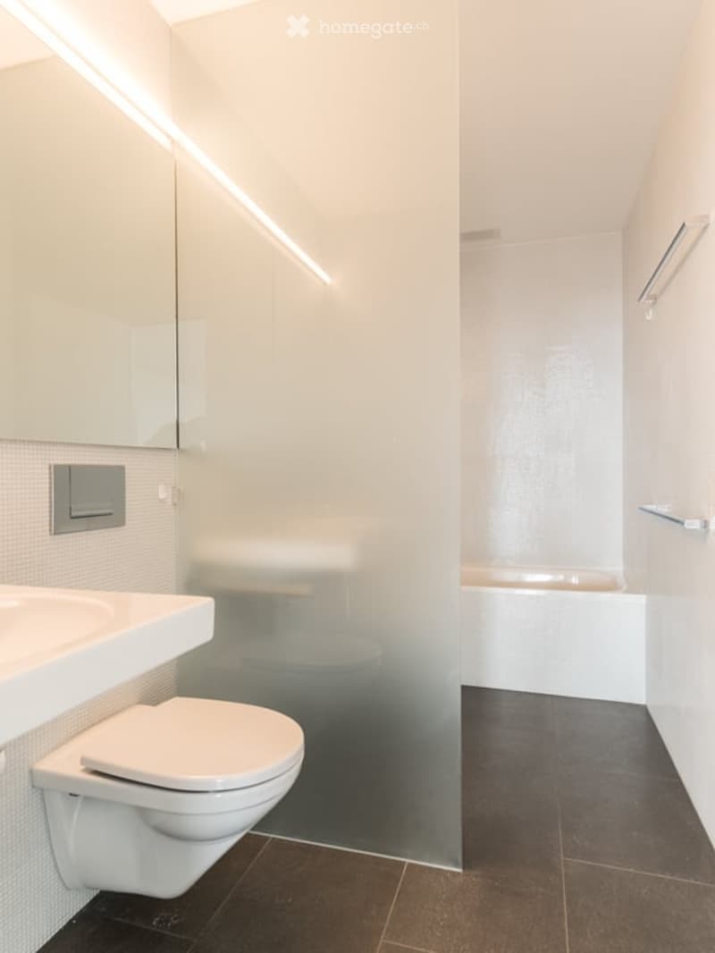 Modern bathroom with a toilet, sink, bathtub, and a large mirrored cabinet. The space features dark tiled flooring and sleek, contemporary design elements.