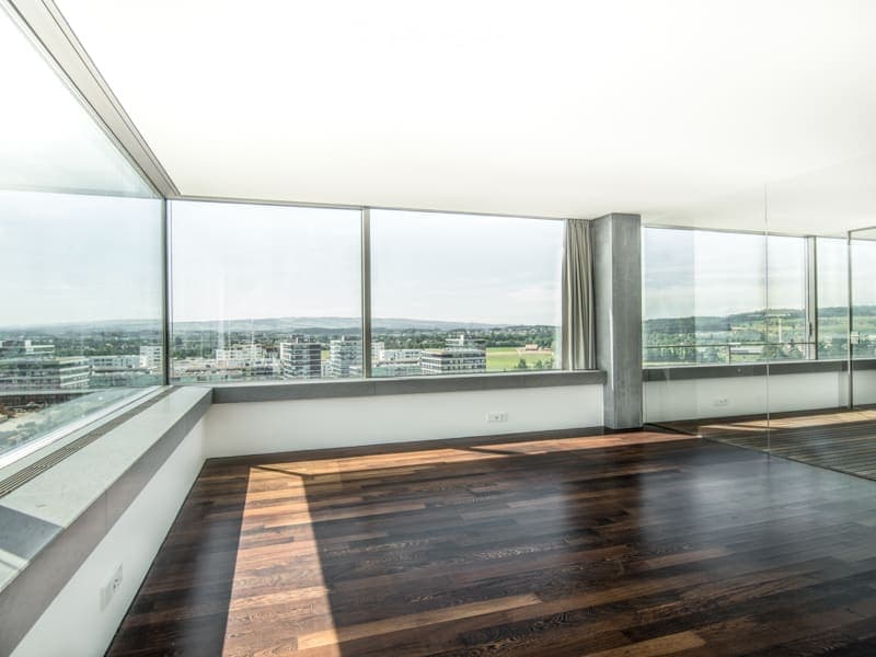 Empty room with large windows, wooden floor, and a view of the cityscape.