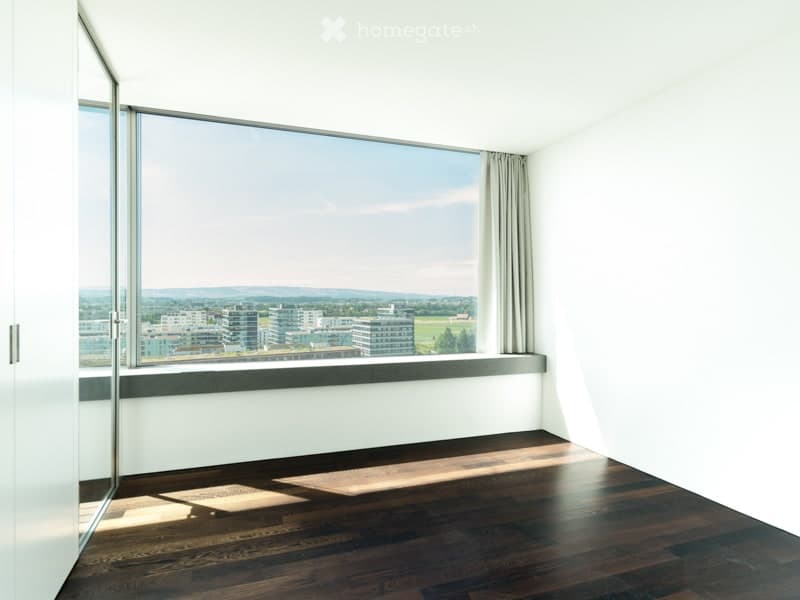Empty room with wooden flooring, large window with view, and white walls.