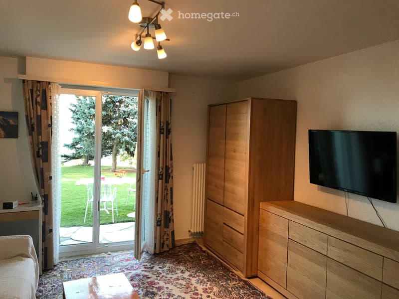 Bright living room with large sliding glass doors leading to a patio, a sofa, coffee table, TV, and wooden cabinet.