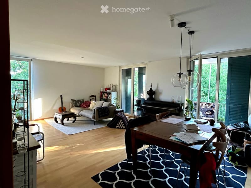 Bright living room with wooden flooring, large windows, a sofa, a dining table, a guitar, and a piano.