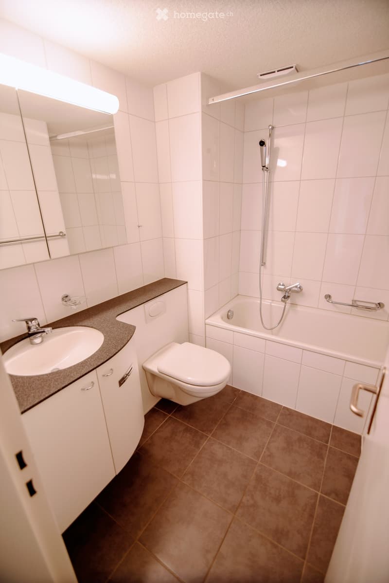 Modern bathroom with white tiles, a sink, toilet, bathtub, and a large mirror above the sink.