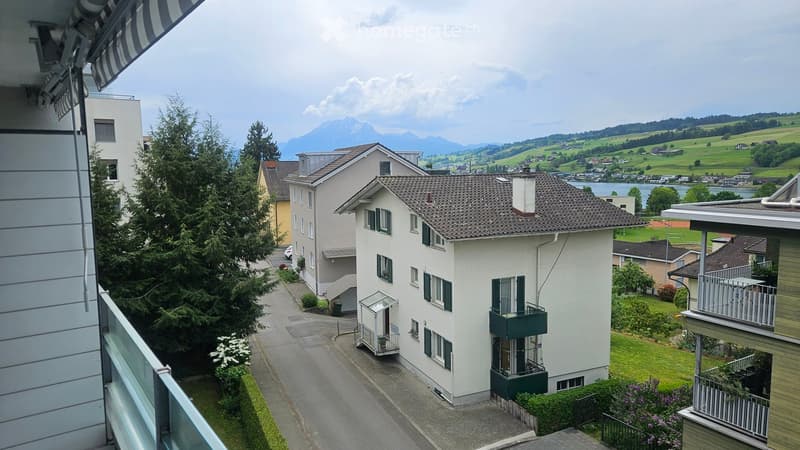View from a balcony showing a residential area with houses, trees, and a scenic mountain backdrop.