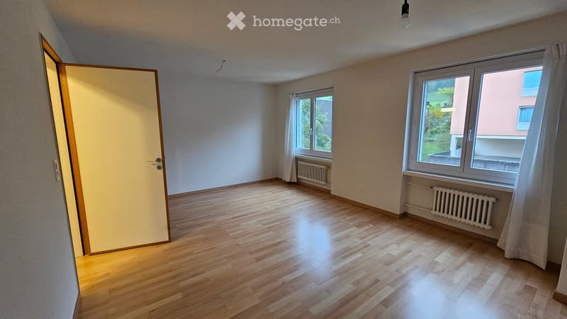 Empty room with wooden floor, white walls, two windows, and a door.