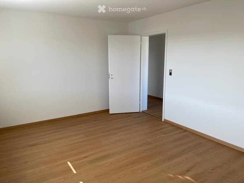 Empty room with light wooden flooring and white walls, featuring a white door leading to another space.