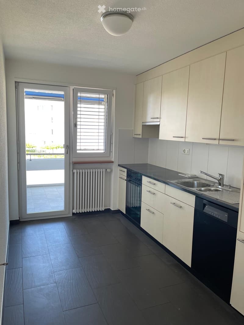 Modern kitchen with white cabinets, dark countertops, and a sink. Features a sliding glass door leading to a balcony.