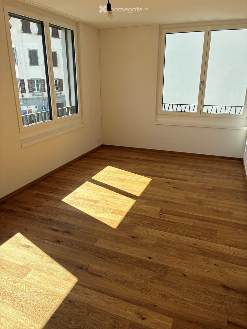 Empty room with wooden flooring, large windows, and natural light. No furniture or equipment present.