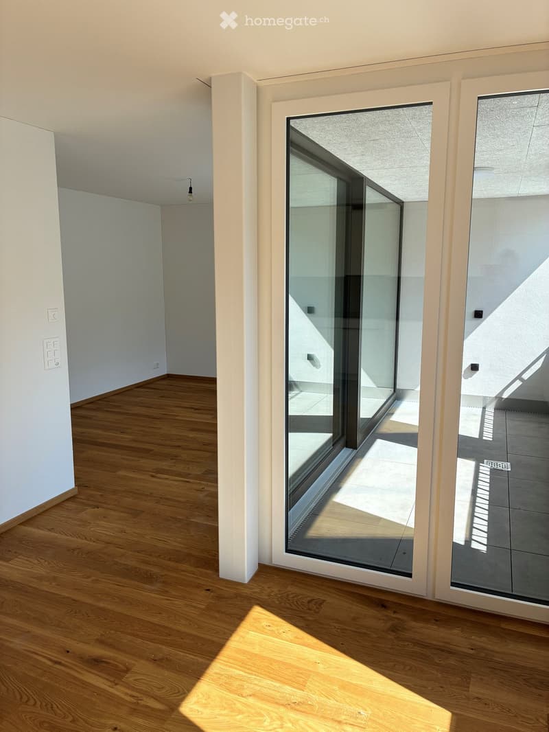 Empty room with wooden flooring, white walls, and large glass sliding doors leading to a balcony area.
