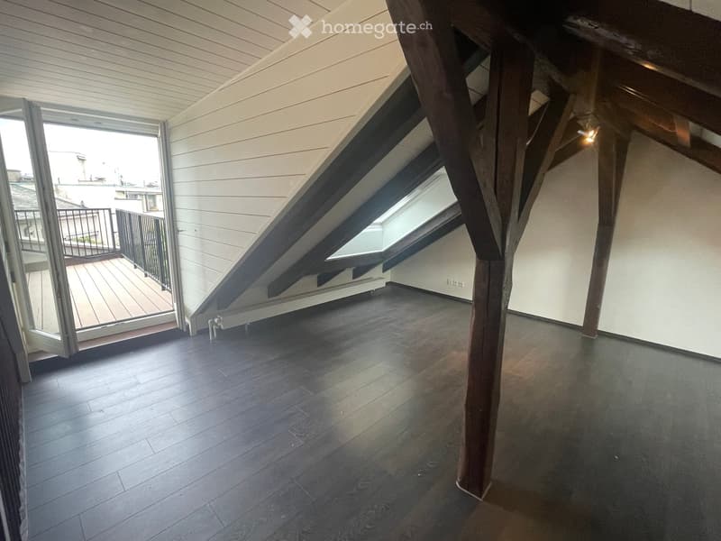 Empty attic space with wooden flooring, exposed wooden beams, skylight window, and access to a balcony.