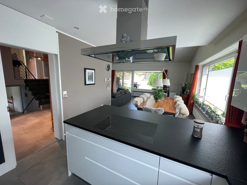 Modern kitchen and living area with white cabinets, black countertop, induction cooktop, dining table with chairs, sofa, and decorative items.