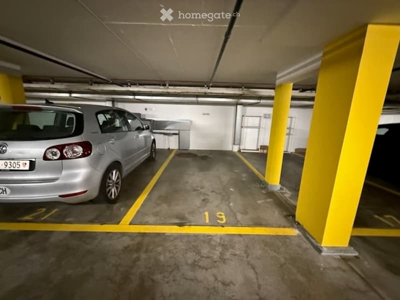 Underground parking area with marked parking spaces, yellow pillars, and a parked car.