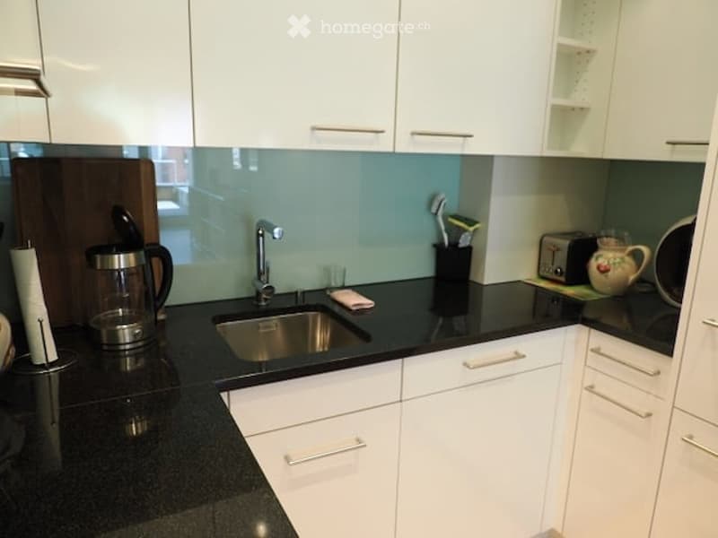 Modern kitchen with white cabinets, black granite countertops, stainless steel sink, coffee maker, toaster, teapot, and a toothbrush holder.