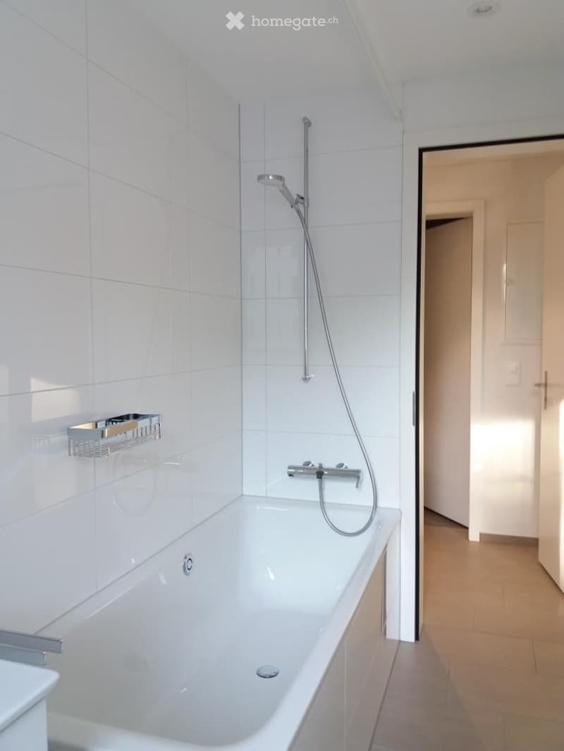Modern bathroom with a white bathtub, a handheld showerhead, a towel rack, and white tiled walls.