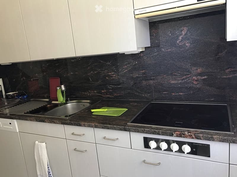 Modern kitchen with white cabinets, dark granite countertops, stainless steel sink, electric stove, and built-in oven.