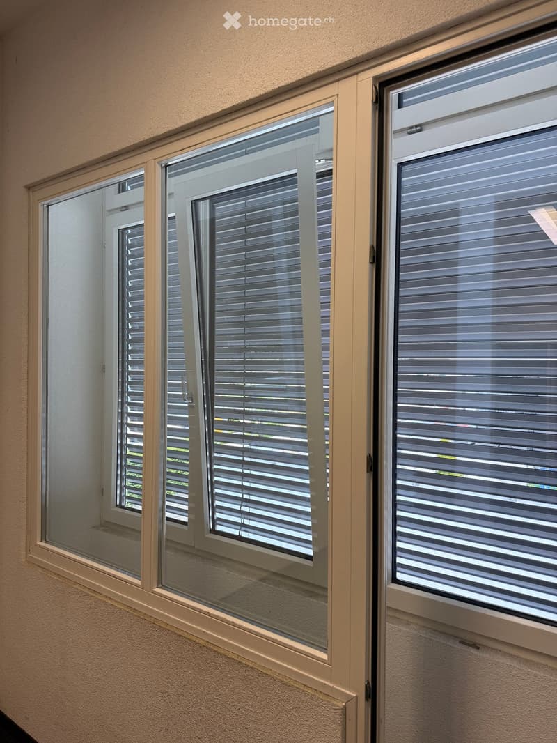 Three windows with blinds in a hallway, featuring white frames and beige walls.