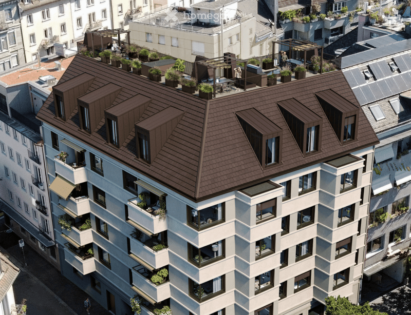 A modern multi-story residential building with a brown tiled roof, multiple balconies, and rooftop terraces. Balconies feature potted plants and outdoor furniture. The building is surrounded by other structures in an urban setting.
