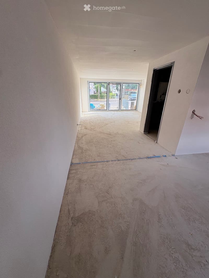Empty room with unfinished concrete floor and white walls, featuring a doorway leading to an outdoor area with glass doors.
