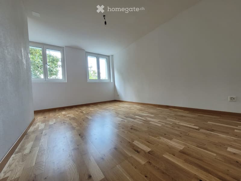 Empty room with wooden flooring, white walls, and multiple windows allowing natural light.