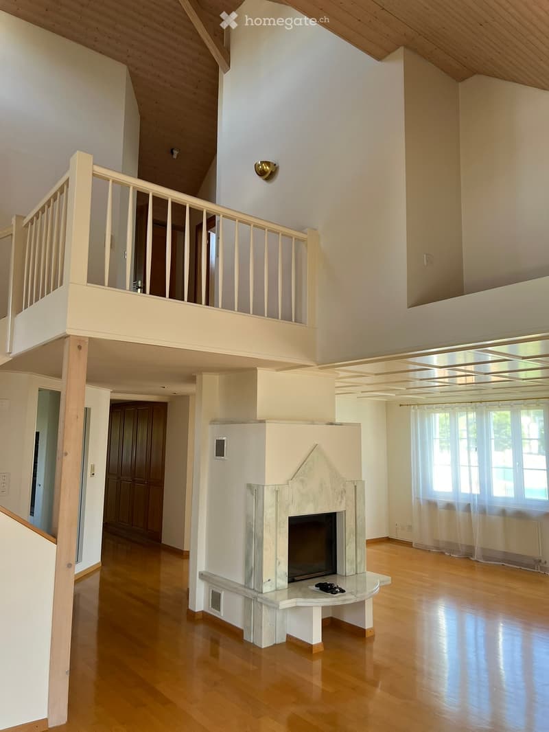 large open room, wooden floor, marble fireplace, balcony above, large windows, wood paneling