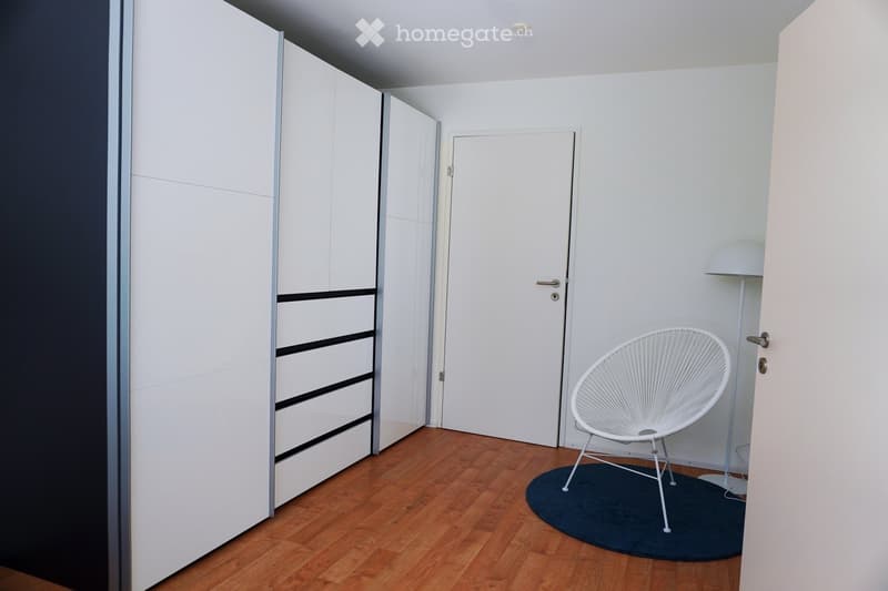Minimalist room with wooden flooring, white wardrobe, and a single white chair on a dark rug.