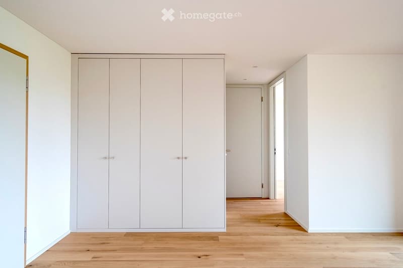 Completely empty room with light-colored walls, wooden flooring, and a large built-in wardrobe unit.