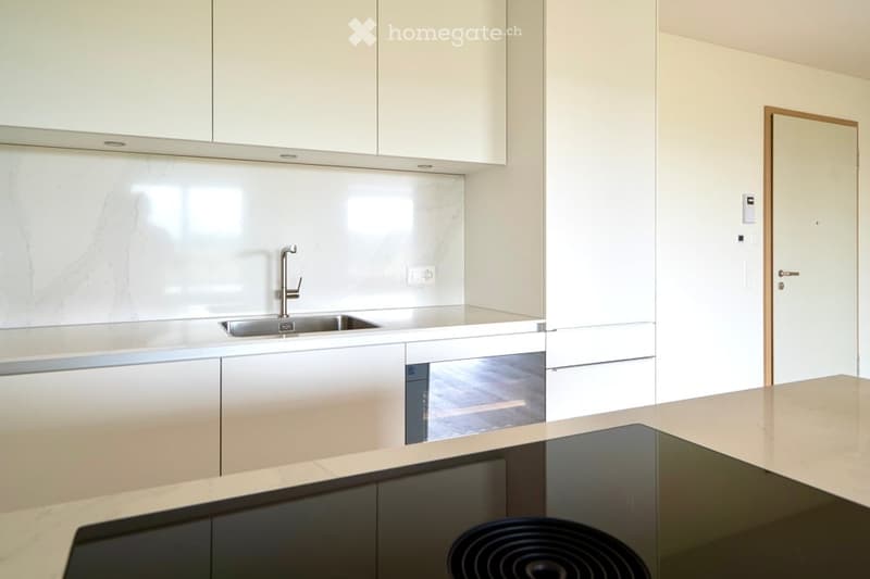 Modern kitchen with white cabinets, marble backsplash, stainless steel sink and faucet, and an electric stove on a light countertop.