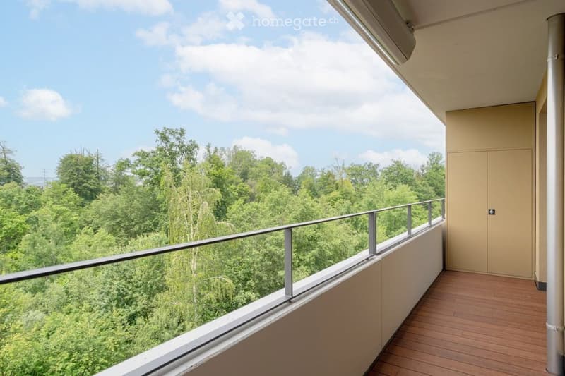 Balcony with wooden flooring, metal railing, and a scenic view of lush green trees.