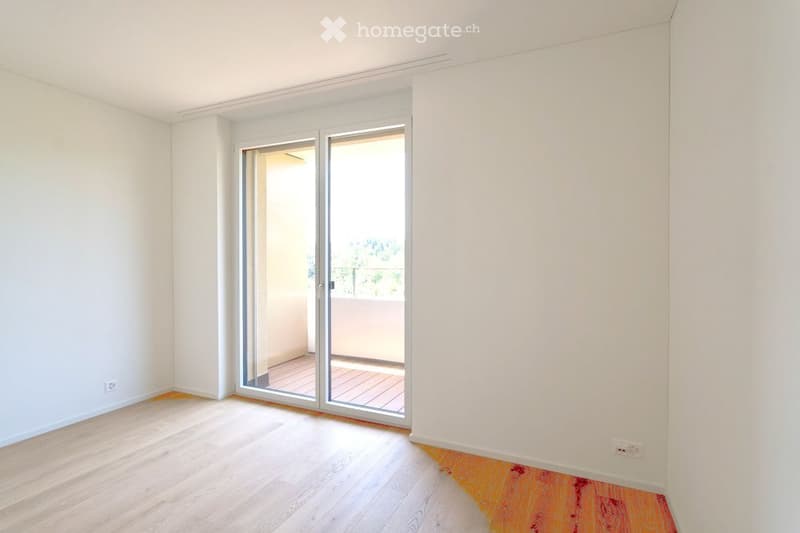 Empty room with light wooden flooring, white walls, and a sliding glass door leading to a small balcony with wooden decking.