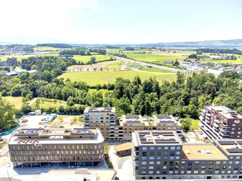 Aerial view of a modern residential complex with multiple buildings, surrounded by green spaces and a road network.