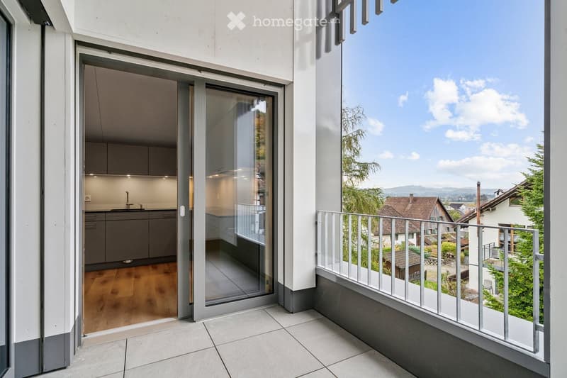 Balcony with sliding glass door, wooden floor, kitchen with sink and cabinets, metal railing, view of houses and mountains