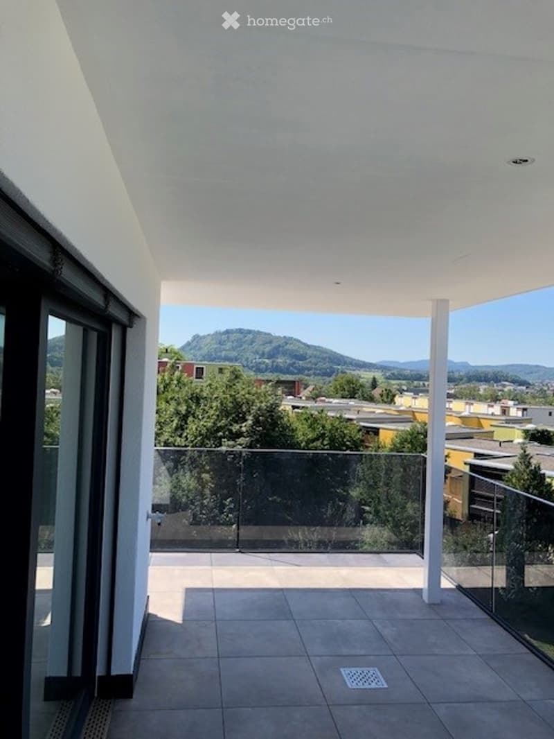 Modern balcony with glass railing, tiled floor, and scenic mountain view.
