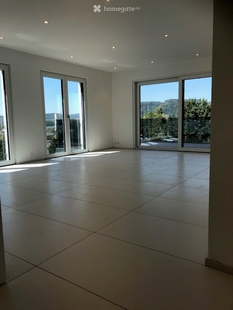 Bright, empty room with large floor-to-ceiling windows offering a scenic view, tiled floor, and recessed lighting.