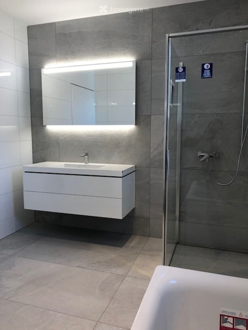 Modern bathroom with a white vanity, built-in sink, large mirror with LED lighting, and a glass-enclosed shower stall.