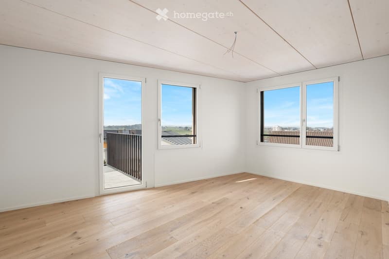 Empty room with white walls, wooden floor, and large windows offering a scenic view. Features a sliding door leading to a balcony.