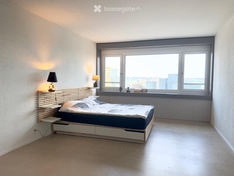 Modern bedroom with a large window offering a city view, a wooden bed with built-in storage, bedside tables with lamps, and a few decorative items on the windowsill.