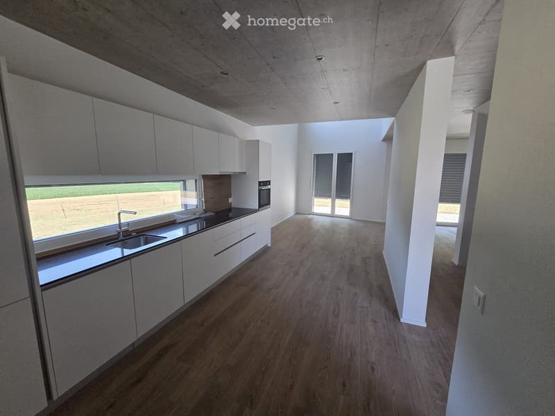 Modern kitchen with white cabinets, wooden flooring, and large windows. Features a sink, faucet, and oven.
