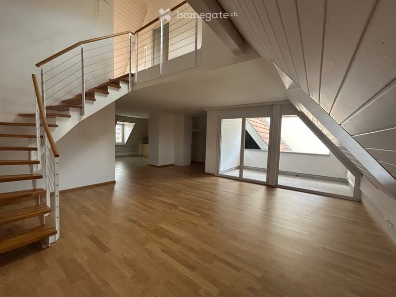 Empty room with wooden flooring, staircase leading to an upper level, and large windows providing natural light.