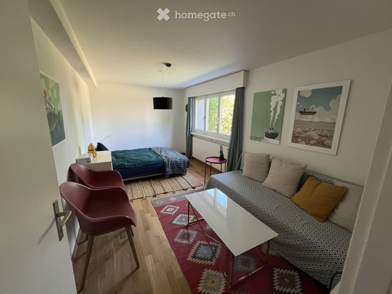 A modern, compact living space with a sofa, coffee table, two chairs, a bed, and artwork on the walls.