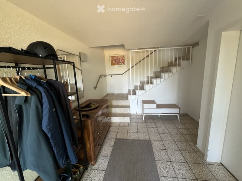 Hallway with tiled floor, coat rack, small bench, and staircase leading upwards.