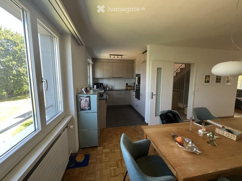 Open-plan kitchen and dining area with modern cabinets, stainless steel appliances, and a wooden dining table with chairs.