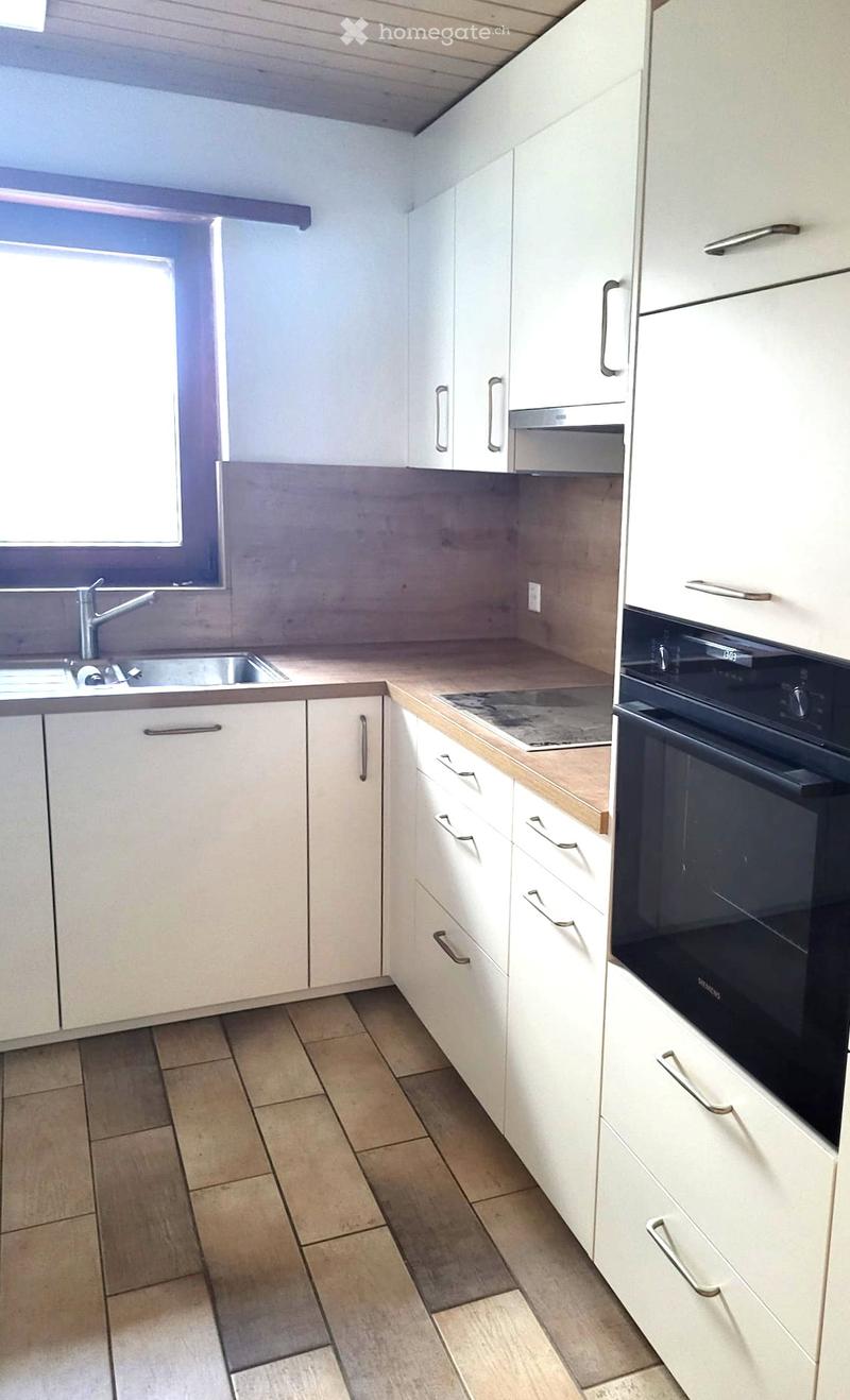 Modern kitchen with white cabinets, stainless steel sink, and built-in oven. Light wood countertops and tiled flooring.