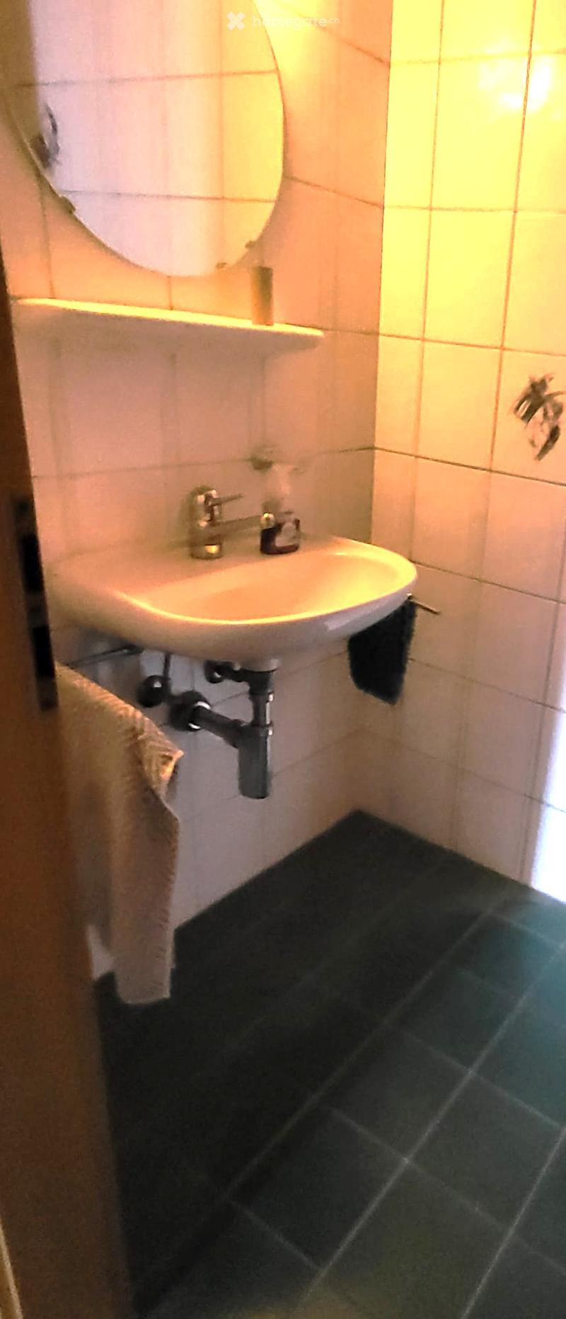 Small bathroom with a white sink, silver faucet, round mirror, and a towel hanging on the side.